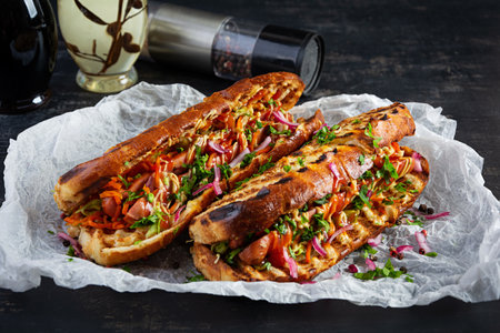 Hot dog with grilled sausage, onion, pickled cucumber, cabbage and spicy carrot. Fast food hot dog with brioche bunの写真素材