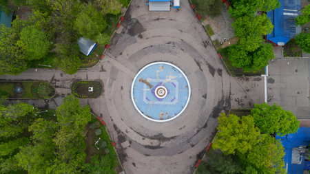 Large fountain is surrounded by trees and a path. The fountain is empty and the trees are green.の写真素材