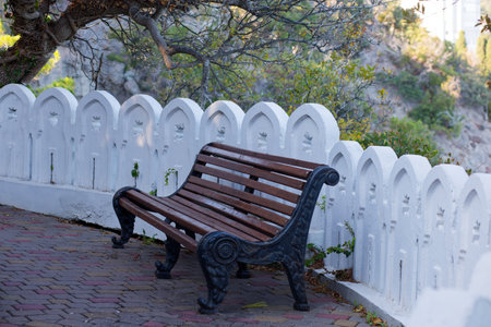 Wooden bench on the promenade in the park with white fenceの写真素材