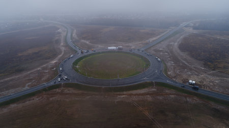 Large circle of road is shown with a foggy atmosphere. The road is surrounded by trees and buildings