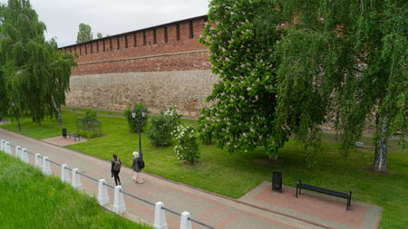 Woman and a man walk down a path in a park. The path is lined with trees and benchesの写真素材
