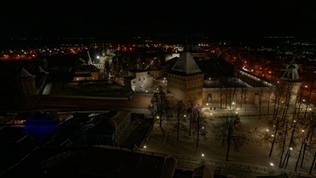 City at night with a large building in the center. The lights are on and the snow is covering the...