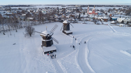 Snowy landscape with two windmills and a small town in the background. The windmills are covered in...