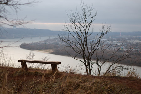 Bench is on a hill overlooking a river. The bench is empty. The sky is cloudy and the trees are bare. Nizhny Novgorod regionの写真素材