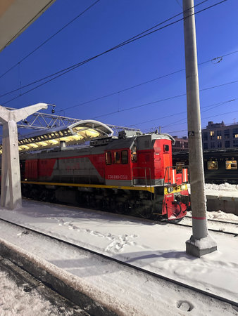 Red train is sitting on the tracks at night. The train is surrounded by snow and the sky is dark....