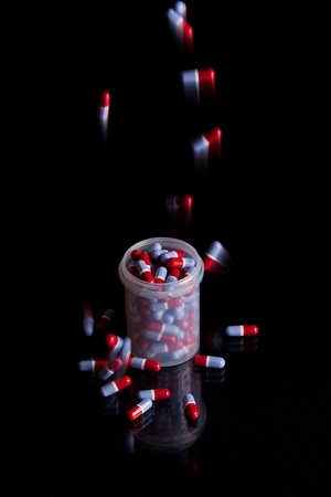 Filling a container already full of capsules - isolated on black backgroundの写真素材