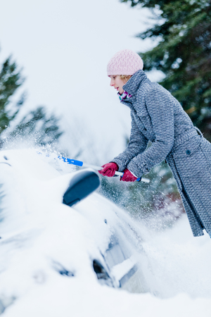Woman Removing Snow from a Car with a Broom after the Blizzardの写真素材
