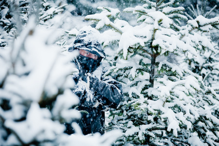 Man Hiding Behind Trees in Forest during a Cold and Snowy Winter Dayの写真素材