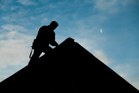 Contractor in Silhouette working on a Roof Top with blue Sky in Backgroundの写真素材