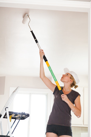 Closeup of Woman Holding Roller Pin and Painting the Ceilingの写真素材