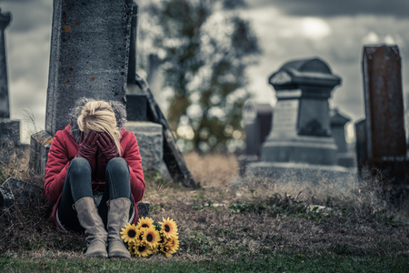 Lonely Crying Young Woman in Mourning with Sunflowers in front of a Gravestone in a Cemeteryの写真素材