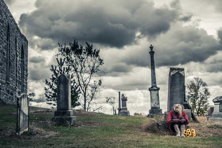 Lonely Sad Young Woman in Mourning with Sunflowers in front of a Gravestone in a Cemeteryの写真素材