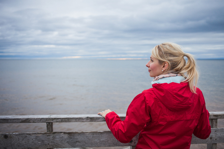 Lonely Young Woman Looking a the View of the Ocean from an Observatory During a cold Autumn Cloudy Dayの写真素材