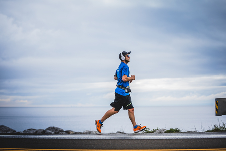 CARLETON, CANADA - June 4, 2017. During the 5th Marathon of Carleton in Quebec, Canada. Young Man Marathoner at about 7km of distance Alone on the side of the Road and Oceanのeditorial素材