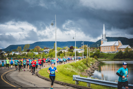 CARLETON, CANADA - June 4, 2017. During the 5th Marathon of Carleton in Quebec, Canada. Marathoners in both sides of the street in a little city with church in backgroundのeditorial素材