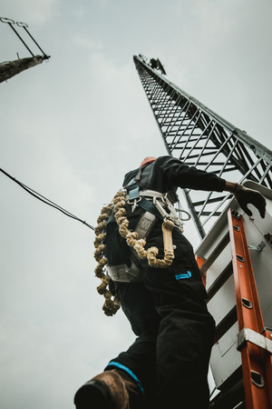 Telecom Worker Climbing Antenna Tower with Tools and Harnessの写真素材