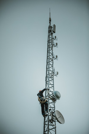 Telecom Worker Climbing Antenna Tower with Tools and Harnessの写真素材