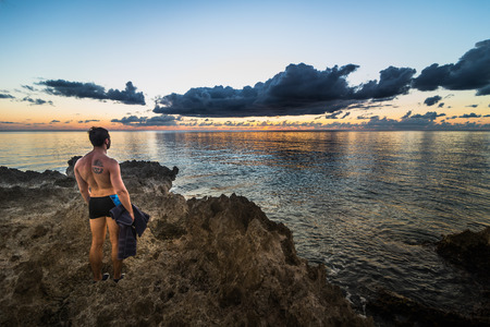 SAN ANDRES ISLAND, Colombia _ Circa March 2017. Man Cheering the Caribbean Sunset Over the Ocean on the Volcanic Rock Shore during the Eveningのeditorial素材