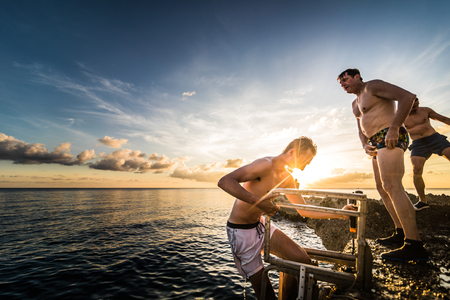 SAN ANDRES ISLAND, Colombia _ Circa March 2017. People Jumping down and coming back up by the ladder a little Volcanic Rock Cliff into the Caribbean Sea of San Andres during a Beautiful Sunset.のeditorial素材