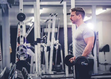Side view of bodybuilder lifting barbell near rows of metal dumbbell in gym.の写真素材
