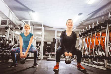 Cheerful confident women training in light gym doing squats with small kettlebells.の写真素材