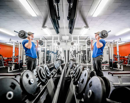 Side view of dumbbells lying in row in gym and man working out with barbell in front of mirror.の写真素材