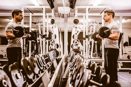 Side view of bodybuilder lifting barbell near rows of metal dumbbell in gym.の写真素材