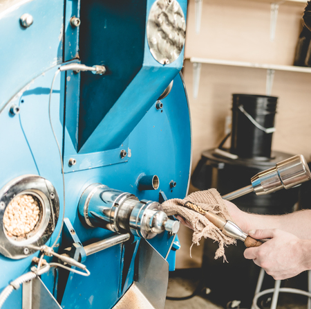 Crop shot of employee taking sample of coffee beans out of roaster machine checking qualityの写真素材
