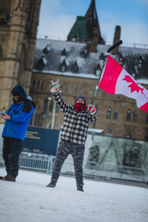 Ottawa, Ontario, Canada - February 12, 2022. Man Waving Flag in Front of Ottawa Parliament during Freedom Convoy Protest in Ottawa.のeditorial素材