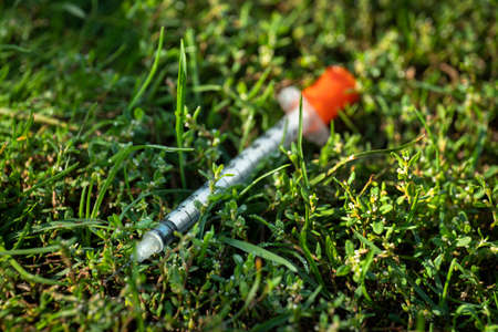 Used syringe hypodermic needle used to inject drugs is discarded on the lawn of a public parkの写真素材