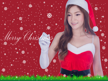 Christmas woman smiling writing merry christmas on screen. Cute beautiful Caucasian santa girl isolated on red backgroundの写真素材