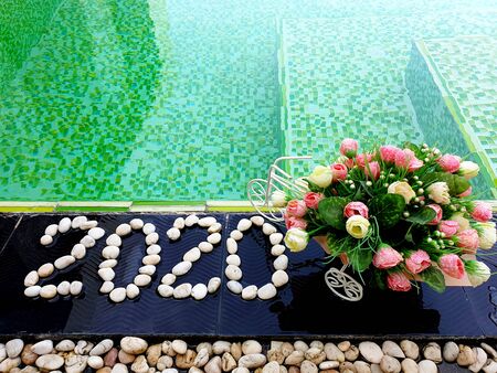 Happy New Year 2020 written by stones on floor tile background with artificial roses flowers close...