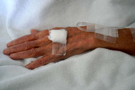Close up hand of old woman patient saline solution in hospital room.