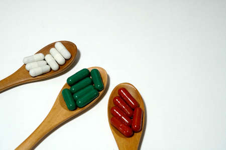 Herbal vitamins in capsule on wooden spoon and white background.