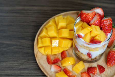 Fresh ripe mango and strawberry fruit in a cup with cookies, soy yogurt in a wooden plate.の写真素材