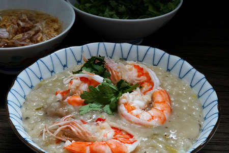 Shrimp Boiled rice soup or shrimp porridge in a bowl with deep-fried garlic and oil, coriander on a wooden table.の写真素材