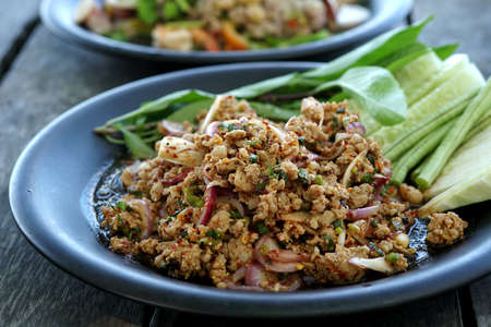 Delicious spicy minced pork salad with fresh vegetables on a plate on a wooden table.の写真素材