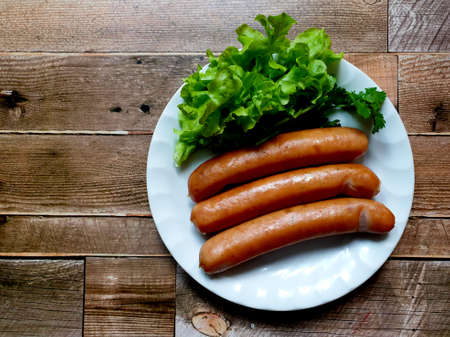 German sausages with green lettuce in a white dish on wooden background.の写真素材