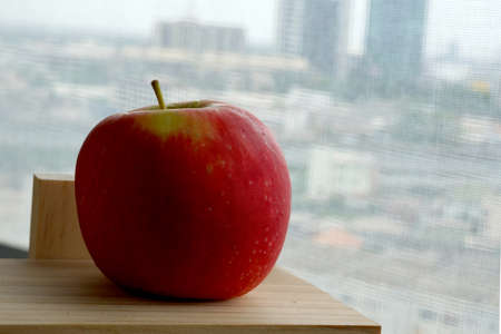 Red apple on wooden shelves near the window of a high building.