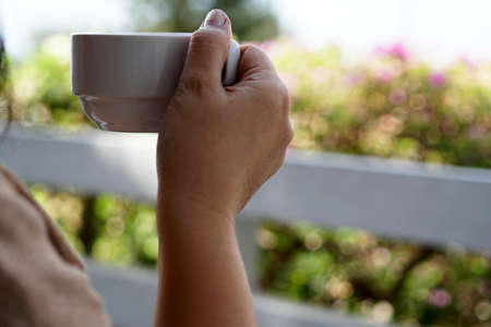 Woman right hand holding a cup of hot coffee during drinking.