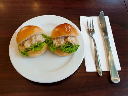 Mini Tuna burgers with mayonnaise salad on a white plate and knife fork on a wooden table.の写真素材