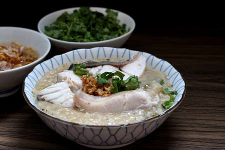 Snapper fish porridge in a bowl and deep fried garlic and oil and coriander on wooden tableの写真素材