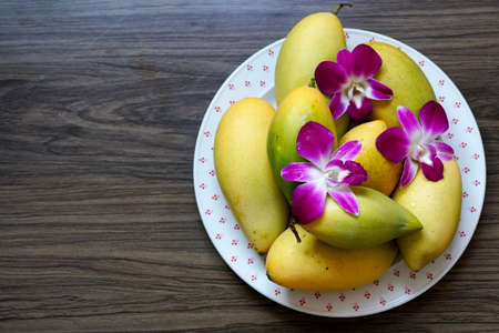 The ripe mango barracuda with decorate dendrobium orchid flower on the plate on wooden background.