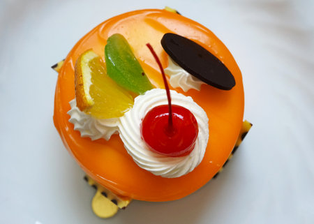 Orange jam cake topped partially whipped cream with red cherry, orange piece, and chocolate plate on...