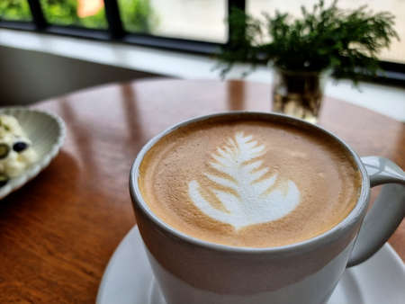 A cup of hot latte art coffee on a wooden table.