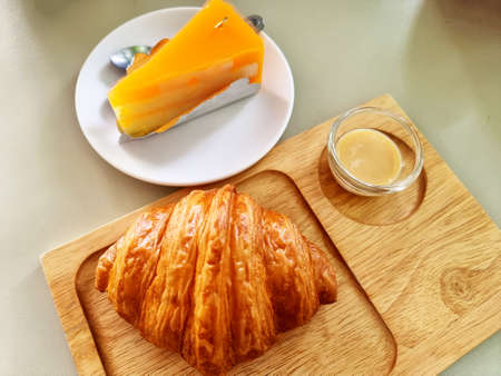 The croissant with sweetened condensed milk on a wooden plate and Orange cake on a white plate.