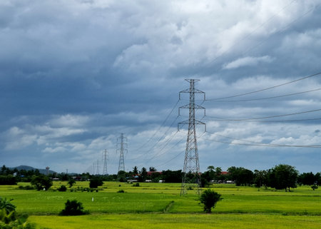 The 230kV transmission line towers on a rice field in the countryside on clouds in the blue sky backgroundの写真素材