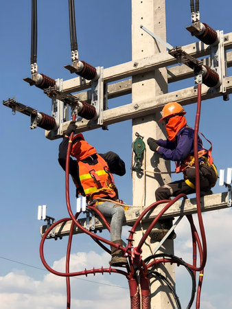 Vertical shot of the electricians working on the electric post power pole for the power cable connecting at the terminal of medium voltage disconnecting switch.の写真素材
