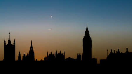Silhouette of the Houses of Parliament and Big Ben at sunset with contrails of overflying planes in the skyの写真素材