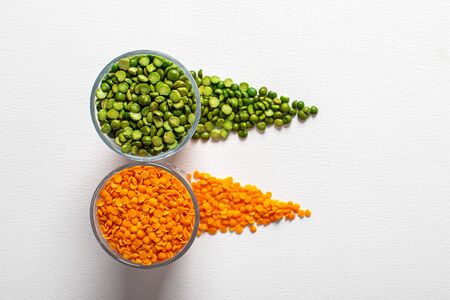 two types of legumes, beautifully arranged in cups and on a white background - green peas and orange...